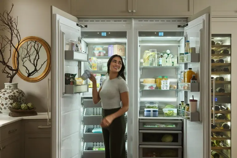 Woman smiling beside an open Viking built-in refrigerator and freezer stocked with food.